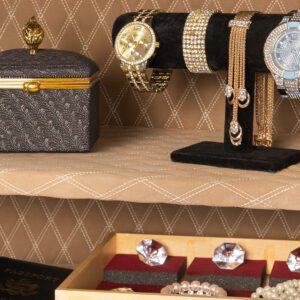 Close-up of the AM3020Plus safe’s interior shelf displaying luxury jewelry, watches, and a decorative box against a quilted tan lining.